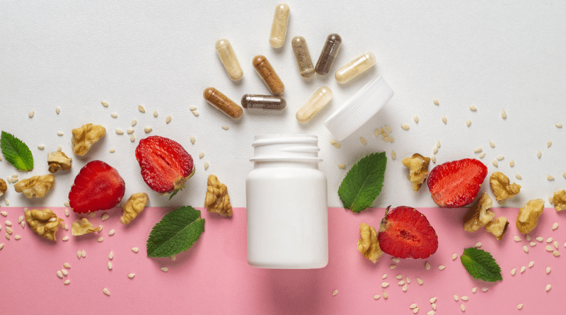 Flat lay of supplement capsules scattered above an open white bottle, with strawberries, walnuts, and mint leaves on a pale surface